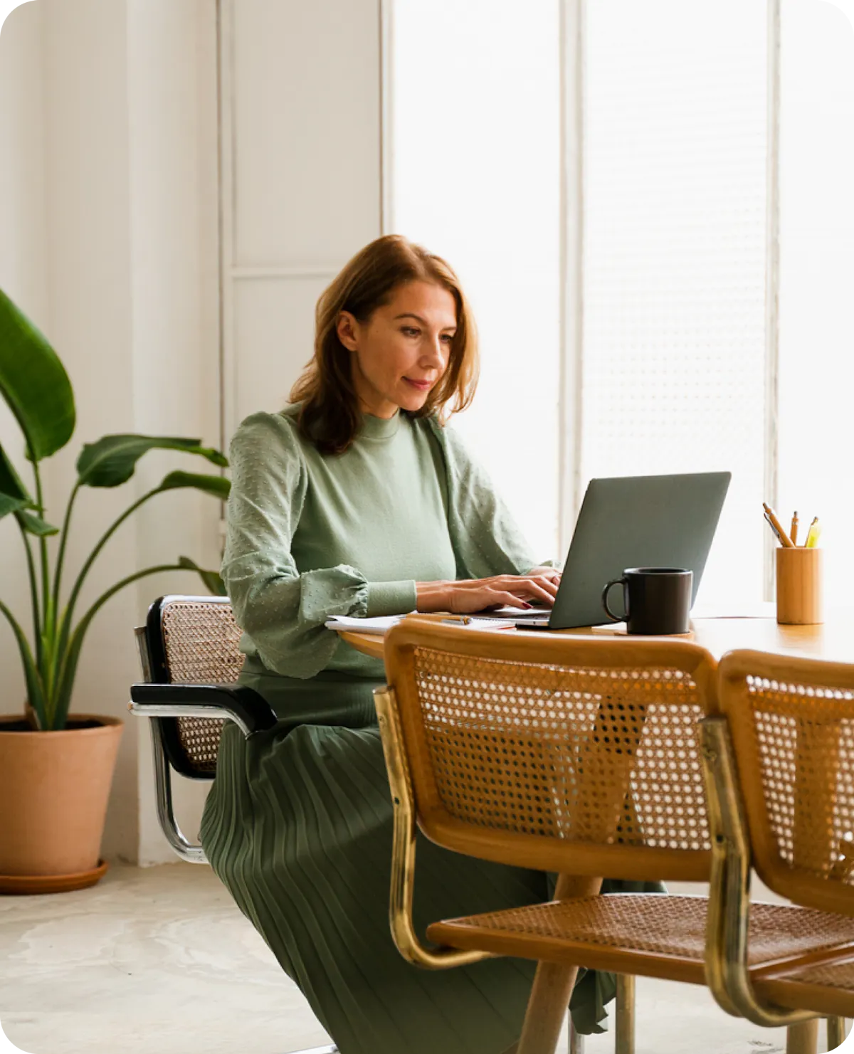 A woman working on a laptop at a table in a bright office.